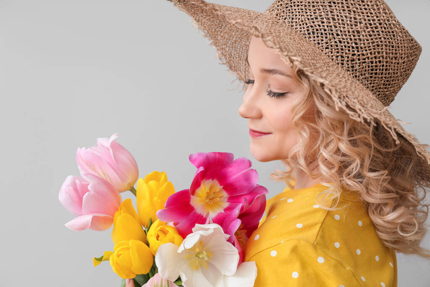 Mooie jonge vrouw met boeket van bloemen op lichte achtergrond - Foto, afbeelding