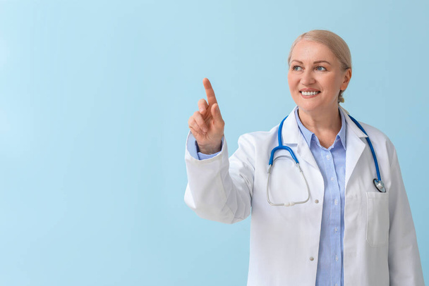 Mature female doctor pointing at something on color background - Φωτογραφία, εικόνα