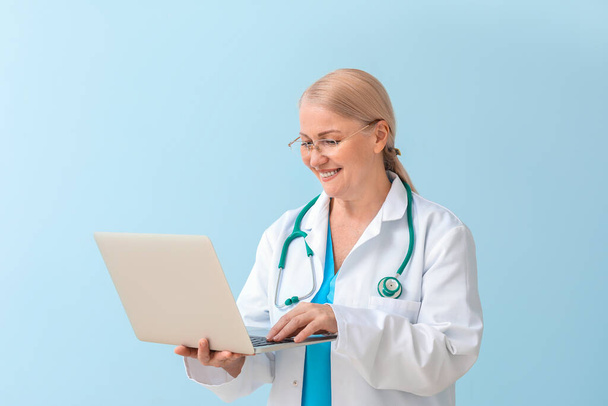 Reife Ärztin mit Laptop auf farbigem Hintergrund - Foto, Bild