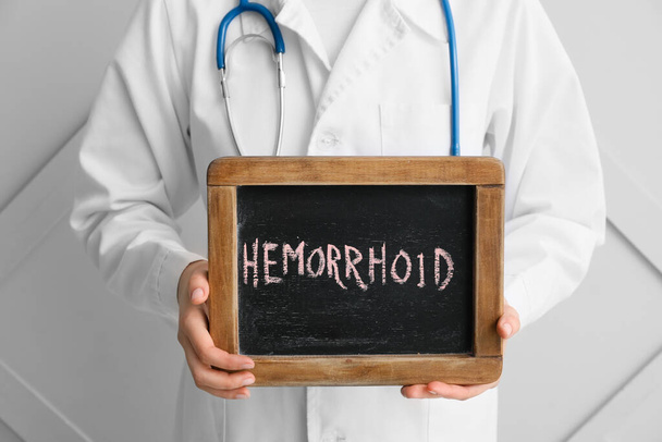 Medico in possesso di lavagna con testo EMORRHOID su sfondo chiaro
 - Foto, immagini