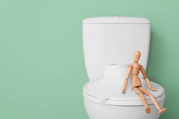 Toilet bowl with paper and wooden human figure on color background - Photo, Image