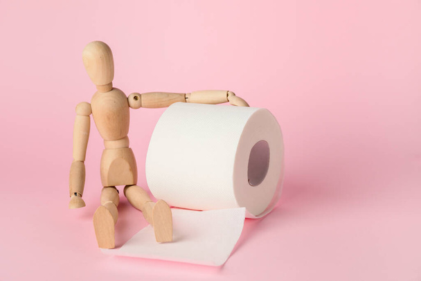 Toilet paper with wooden human figure on color background - Photo, Image