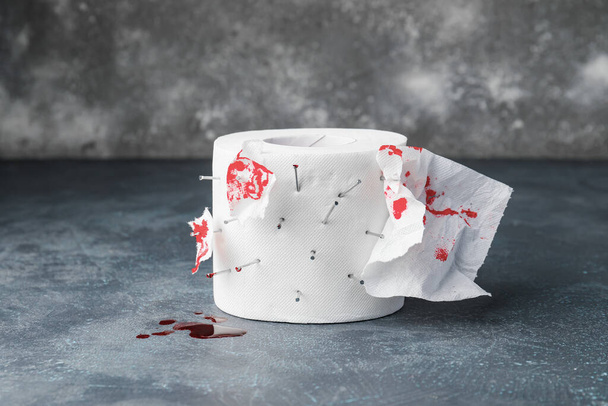 Toiletpapier met spijkers en bloedvlekken op grijze achtergrond. Hemorroïden concept - Foto, afbeelding