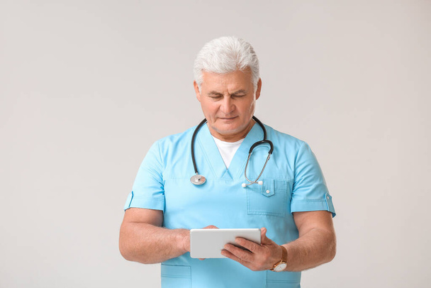 Mature male doctor with tablet computer on grey background - Φωτογραφία, εικόνα