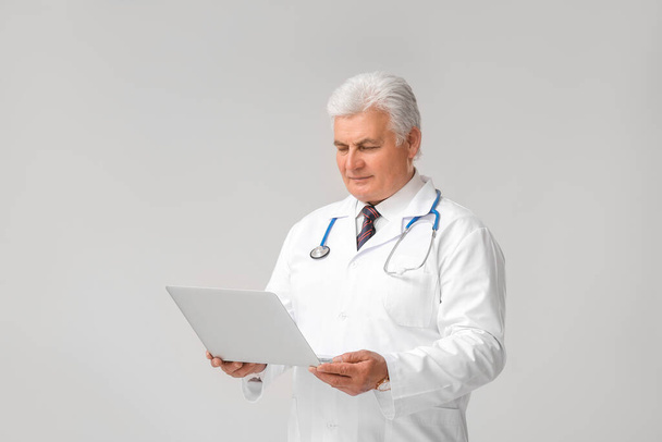 Médico varón maduro con portátil sobre fondo gris
 - Foto, imagen