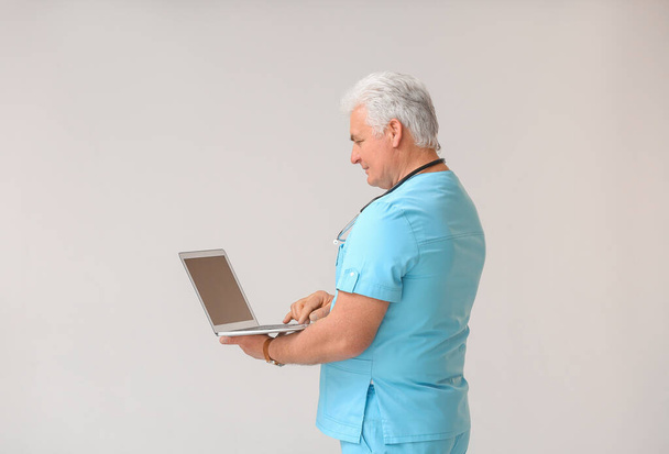 Dojrzały lekarz z laptopem na szarym tle - Zdjęcie, obraz