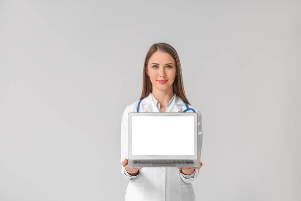 Doctora joven con portátil sobre fondo gris
 - Foto, imagen