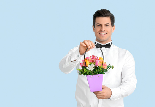 Handsome man with bouquet of flowers on color background - Фото, зображення