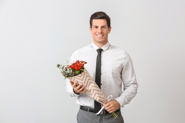 Hombre guapo con ramo de flores sobre fondo claro
 - Foto, Imagen