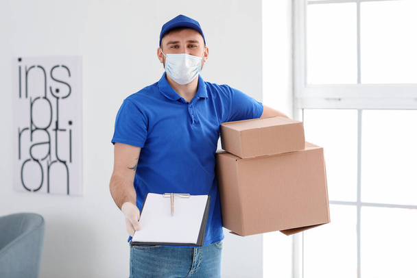 Männlicher Kurier in medizinischer Maske und mit Boxen im Haus - Foto, Bild