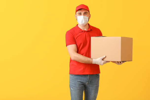 Männlicher Kurier in medizinischer Maske und mit Schachtel auf farbigem Hintergrund - Foto, Bild