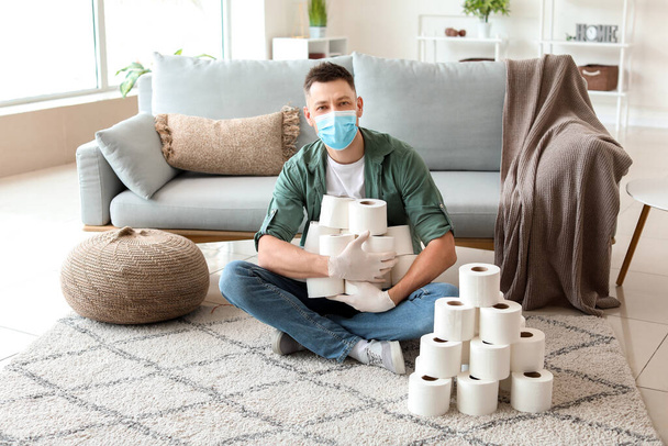 Homem mascarado e com montes de papel higiénico em casa. Conceito de epidemia de coronavírus
 - Foto, Imagem