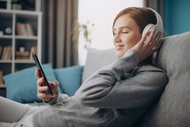 Girl relaxing on couch and enjoying music in headphones - Photo, Image