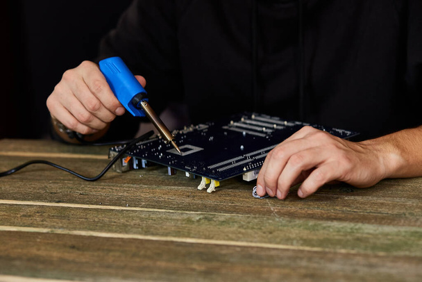 Technician or engineer is focused on repairing electronic circuit board with soldering iron. Man hands soldiers computer circuit board using soldering iron. Copy space. - Photo, Image