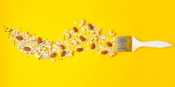 paintbrush with oatmeal and almonds cashew nuts isolated on yellow background, copy space for text, healthy breakfast concept - Photo, Image