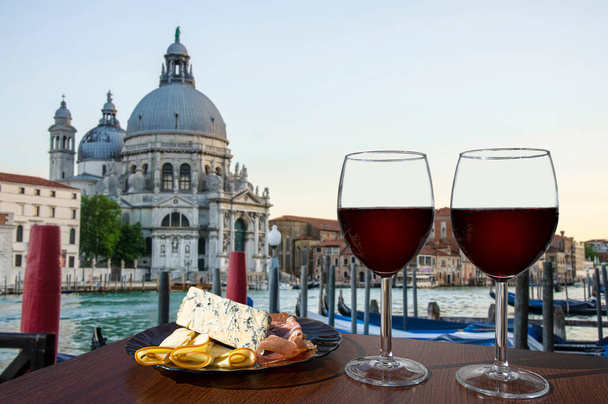 Дві склянки червоного вина з асортиментом з гондол і салюту Санта-Марія-делла. Скло червоного вина з різними перекусками - тарілка з шинкою, нарізаний, синій сир. Пара романтичних свят - Фото, зображення