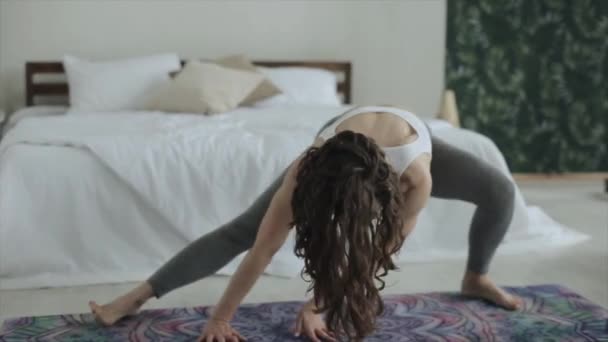 Young attractive girl practices yoga while doing different exercises on the mat in her room in beautiful sportswear - Filmagem, Vídeo