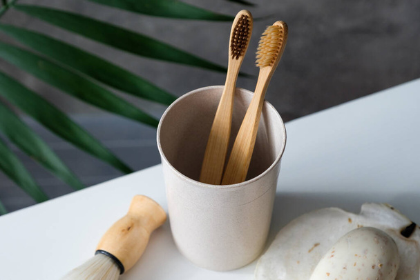 Eco friendly bamboo toothbrushes in glass with shaving brush and organic soap on table in bathroom. Zero waste, plastic free, sustainable lifestyle concept - Foto, Bild