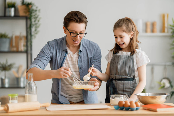 Happy loving family are preparing bakery together. Father and child daughter girl are cooking cookies and having fun in the kitchen. Homemade food and little helper.  - Foto, Imagen
