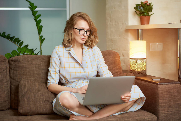 Eine Frau im Kleid, die mit überkreuzten Beinen auf der Couch sitzt, arbeitet ferngesteuert an einem Laptop. Ein ernstes Mädchen mit Zahnspange beobachtet ein Webinar. Eine Studentin mit Brille hört einer Online-Vorlesung zu. - Foto, Bild