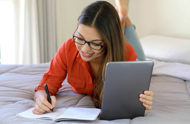 Homeschooling, e-learning, smart school, distant education concept. Smiling student girl wearing glasses studying online comfortable at home. Happy young business woman take notes from webinar. - Photo, Image
