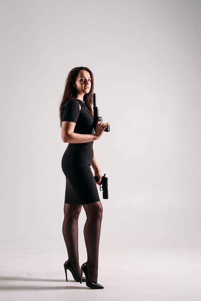 Young girl in a black formal dress with arms in her hands on a white background in the studio, she depicts a bodyguard or Agent - Fotoğraf, Görsel