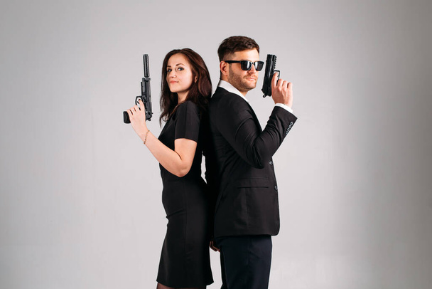 Young girl guy and in black formal suits with arms in their hands on a white background in the studio, they depict bodyguards or agents - Photo, image