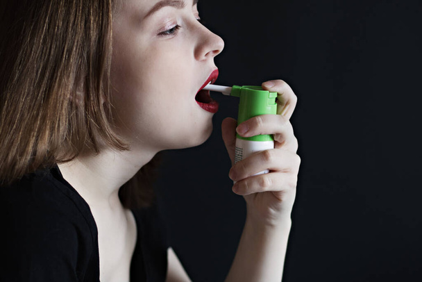 A young woman using a painkiller with an antiseptic spray to soften her throat, remove the pain.Glossy oral spray or aerosol bottle for the prevention and treatment of respiratory infections. Banner. - Photo, Image