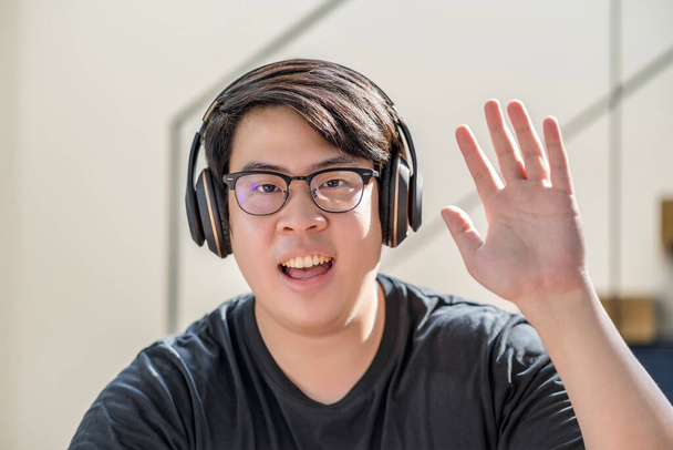Asian business man waving hand for say hello when making video call to friend with social distancing, smiling female taking video blog recording vlog, Covid-19 pandemic, headphone and online meeting - Photo, Image