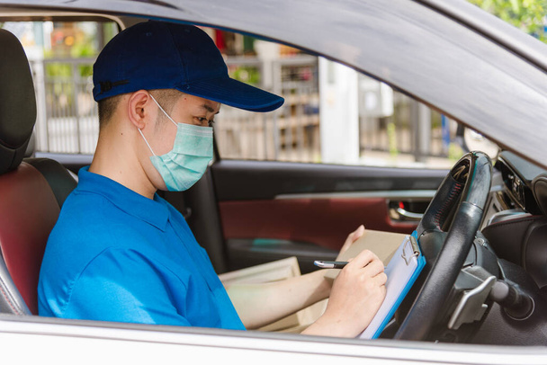 Asian delivery courier young man driver inside the van car with parcel post boxes checking amount he protective face mask, under curfew quarantine pandemic coronavirus COVID-19 - 写真・画像
