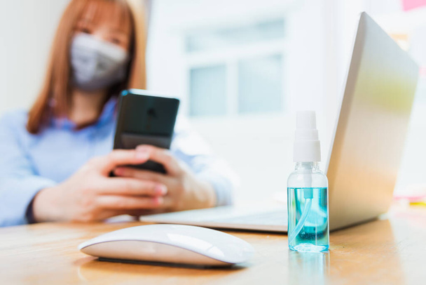 Asian young business woman wearing face mask protective using smart mobile phone for reading SMS message near laptop computer at home office quarantines disease coronavirus or COVID-19, work from home - Valokuva, kuva