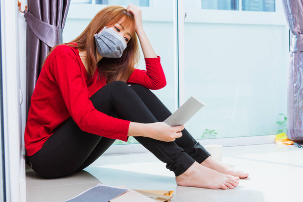 Asian young sad woman hug her knee and cry wearing face mask protective unemployed quarantines disease coronavirus or COVID-19 her sitting alone on floor holding papers unpaid bills debt credit - Zdjęcie, obraz