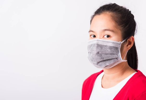 Asian adult woman wearing red shirt and face mask protective against coronavirus or COVID-19 virus or filter dust pm2.5 and air pollution she looking camera, studio shot isolated white background - Fotó, kép