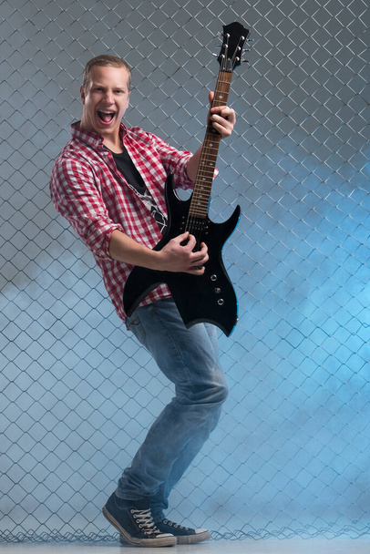 Μουσική, ήχος. Μουσικός με κιθάρα σε φόντο φράχτη - Φωτογραφία, εικόνα