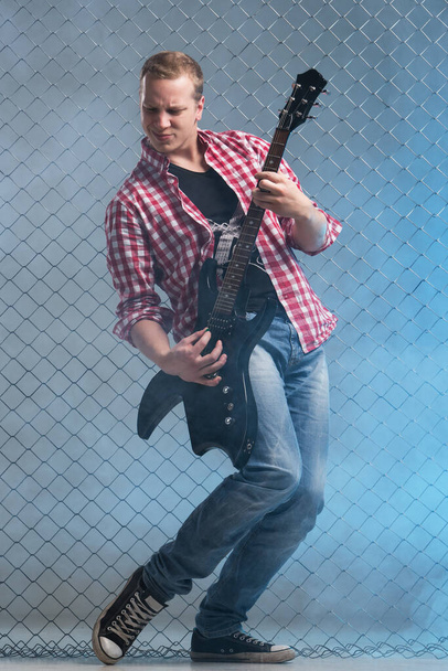 Muziek, geluid. Muzikant met een gitaar op hek achtergrond - Foto, afbeelding