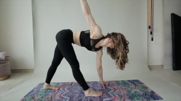 Mladá atletická dívka procvičuje jógu při složitých cvičeních při stání na rukou na podložce v černém sportovním oblečení - Záběry, video