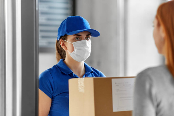 delivery girl in face mask giving parcel to woman - Fotoğraf, Görsel