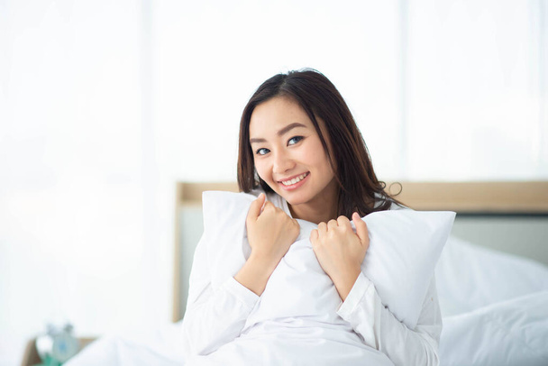Mulher asiática abraçar o travesseiro na cama sorriso e feliz
 - Foto, Imagem