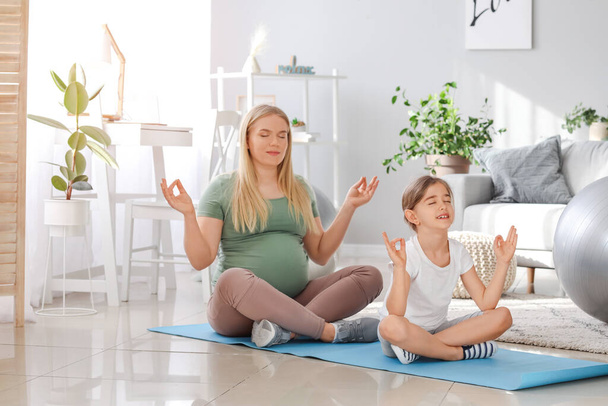 Pregnant woman and her little daughter practicing yoga at home - Photo, Image