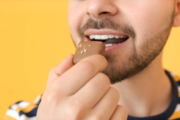 Handsome young man eating tasty chocolate on color background, closeup - Foto, immagini