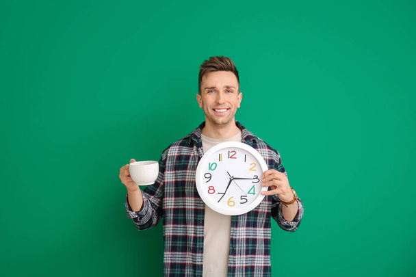 Νεαρός άνδρας με καφέ και ρολόι στο φόντο χρώμα - Φωτογραφία, εικόνα