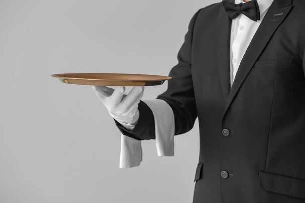 Handsome male waiter with empty tray on grey background - Photo, Image