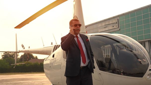 Бізнесмен розмовляє на мобільному телефоні біля приватного вертольота
 - Фото, зображення