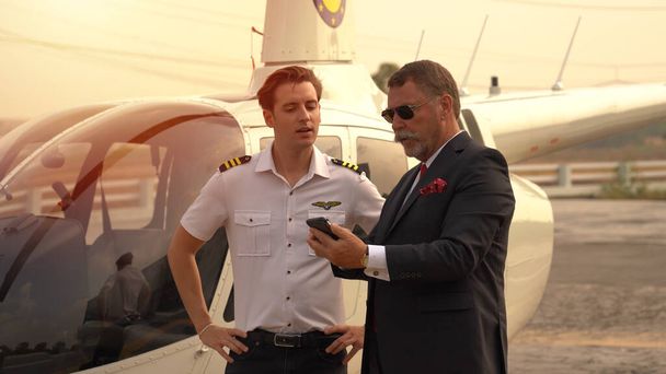 Obchodní muž a pilot mluví v blízkosti malé soukromé helikoptéry na místě přistání - Fotografie, Obrázek