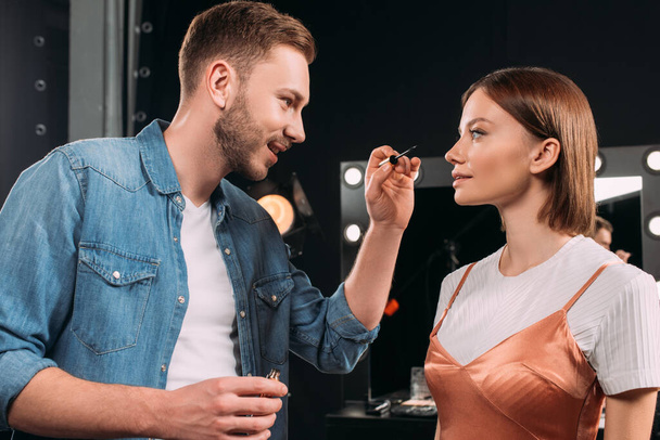 Smiling makeup artist holding mascara near beautiful model  - Fotografie, Obrázek