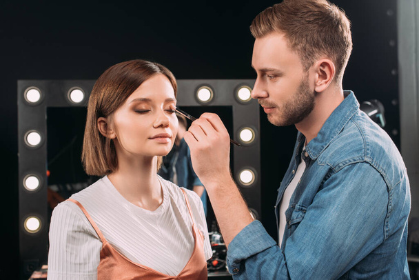 Handsome makeup artist applying eye shadow on model in photo studio  - Foto, Imagen