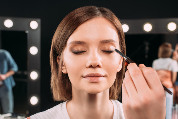 Maquiagem artista segurando escova cosmética ao aplicar sombra nos olhos em modelo bonito
  - Foto, Imagem