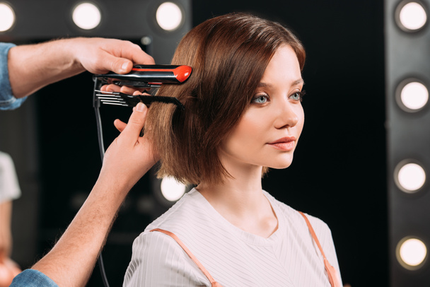 Makeup artist using curling iron on attractive model in photo studio  - Photo, Image