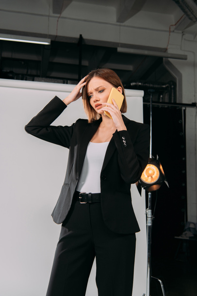 Upset elegant model talking on smartphone in photo studio  - Fotó, kép