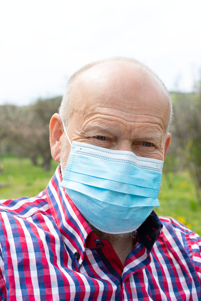 Portrait of elderly man with surgical mask spending time outdoors in the garden  - Photo, Image